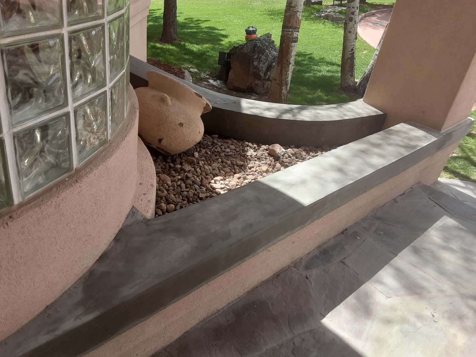 Smooth troweled concrete garden wall cap beside river rock